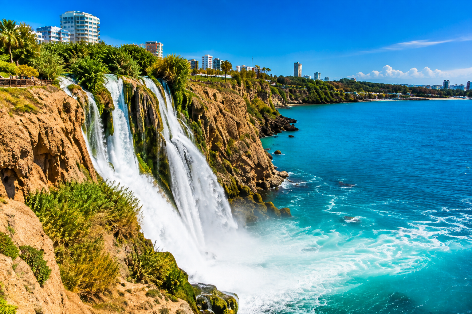 Düden Waterfalls cascading from the cliffs into the turquoise Mediterranean Sea near Antalya, surrounded by lush greenery and dramatic coastal scenery.