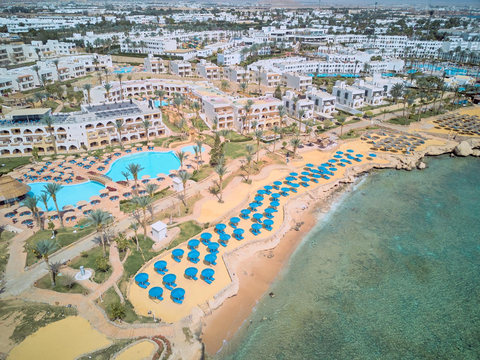 A luxurious beachfront resort in Sharm El Sheikh overlooking crystal-clear turquoise waters, palm trees and the Red Sea coastline.